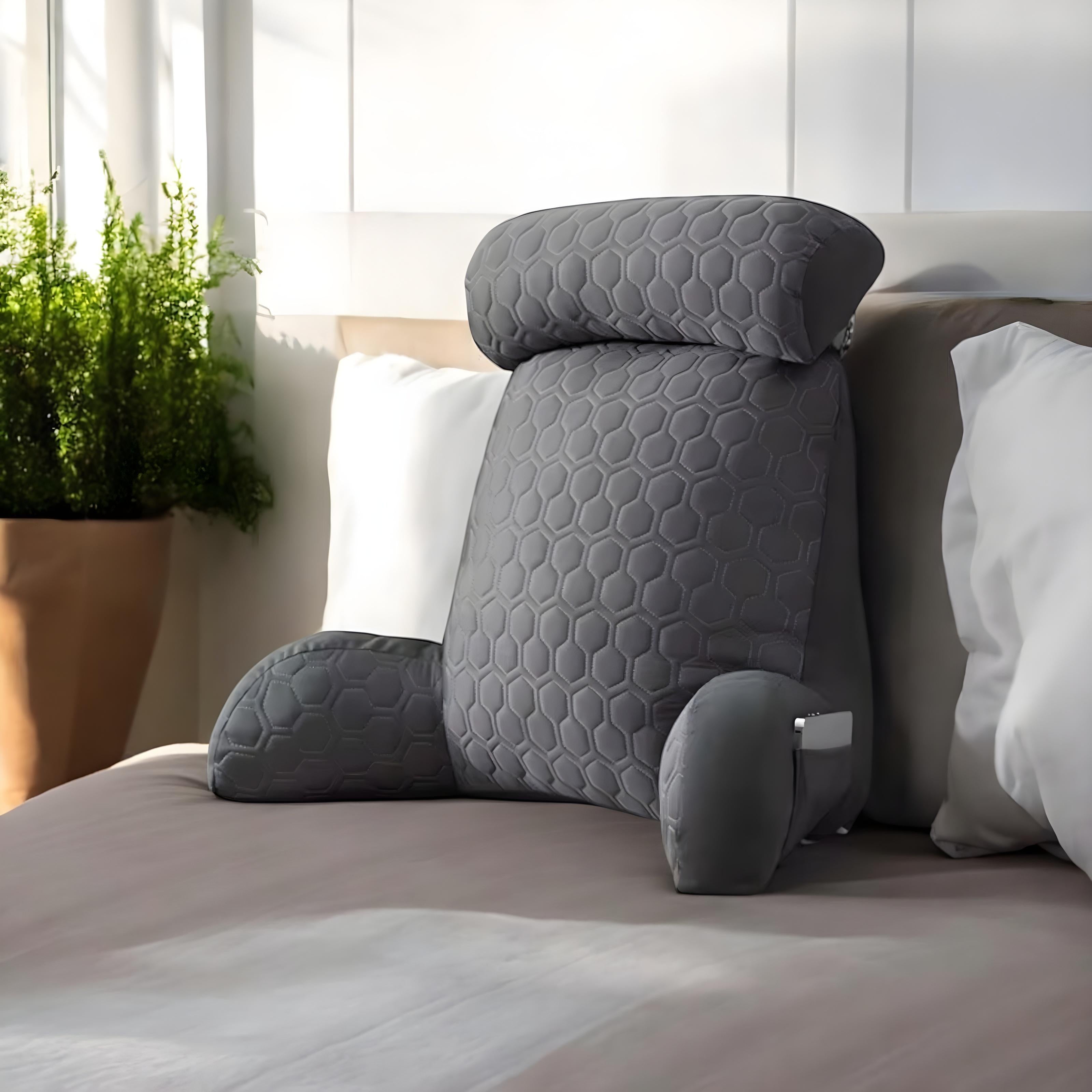 Reading cushion on a comfortable bed with a plant pot next to the bed.